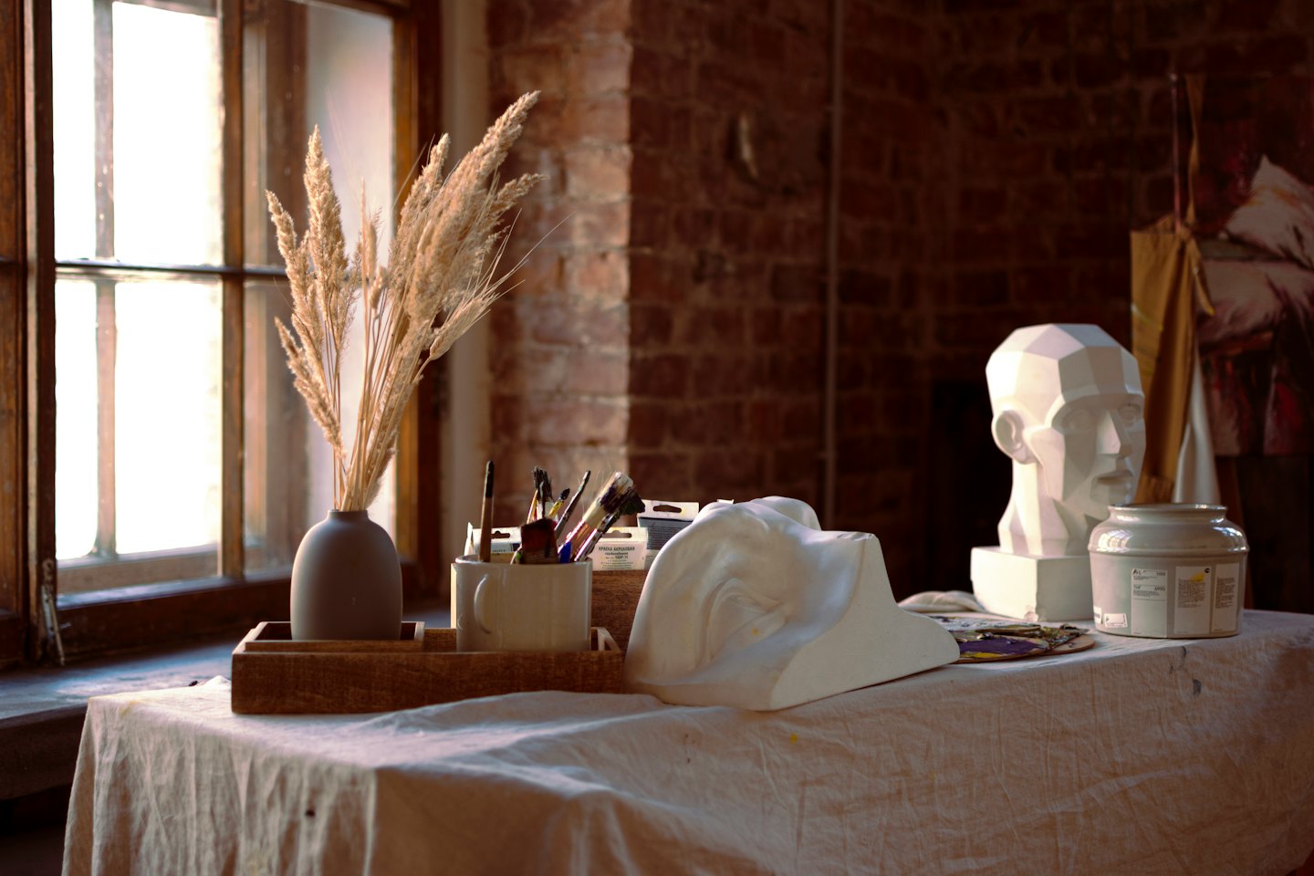 Artist's studio window light falls on a table with vase and plaster casts.