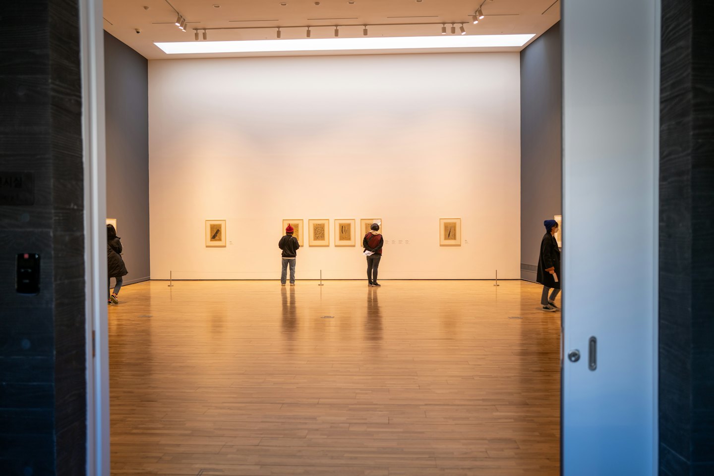 Visitors observe framed art on a white wall in a gallery.