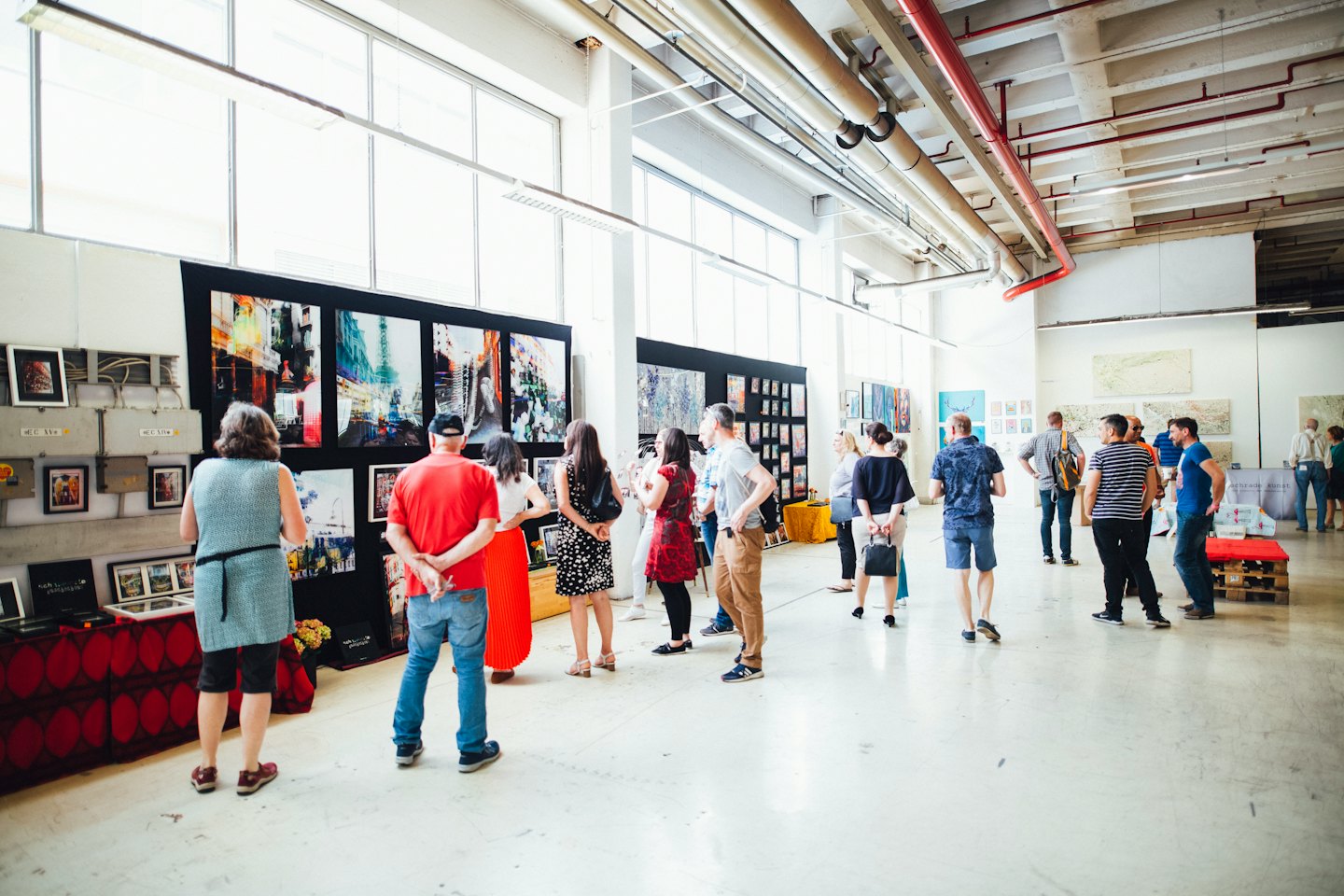 People viewing paintings and photographs in a modern art gallery.