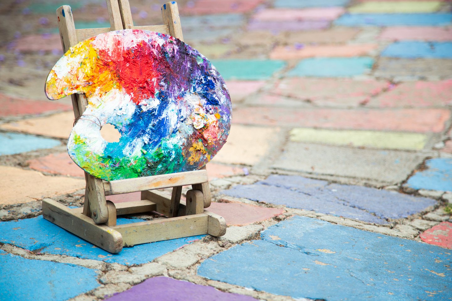 Wooden easel with colorful paint palette on stone patio.