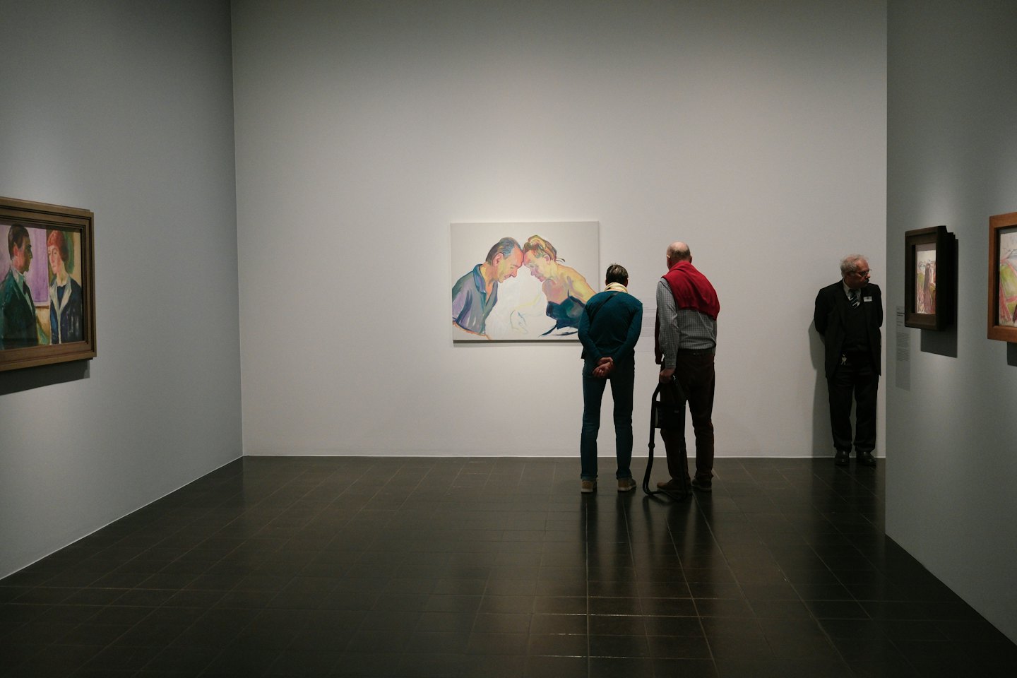 People viewing framed paintings in a modern art gallery.